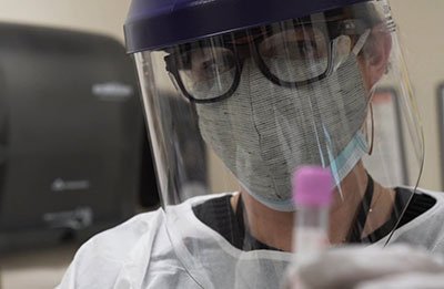 A nurse in personal protective gear holds up a vial of vaccine.