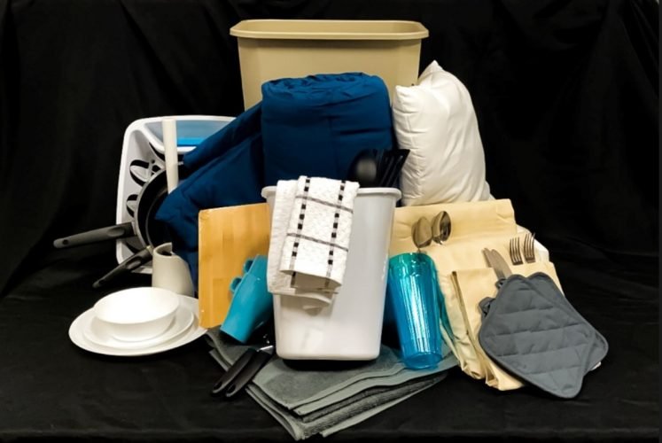 An assortment of housewares, including a garbage can, cup and saucer, drinking glass, towels, kitchen towels, cutlery, hot pads, sheets an more.